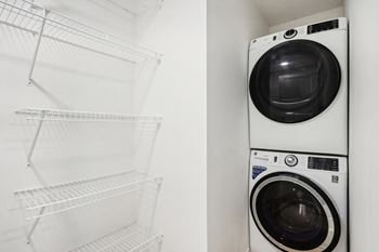 A white dryer is stacked on top of a white washer in a white laundry room.